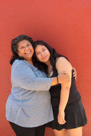 Single mother and her 18-year-old Latina daughter show their love with kisses and hugs and celebrate...