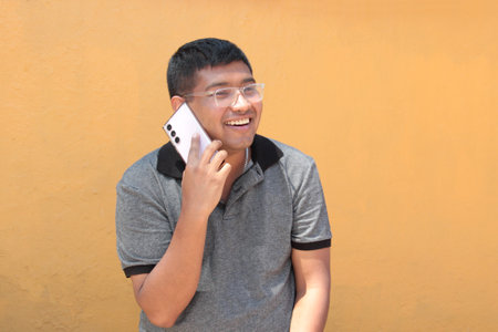 30-year-old dark-skinned Latino man with glasses uses his cell phone to work remotely, make calls,...
