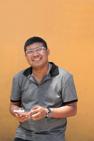 30-year-old dark-skinned Latino man with glasses uses his cell phone to work remotely, make calls,...