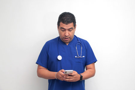 Dark-skinned Latino male doctor with a stethoscope shows his cell phone to have online consultations...