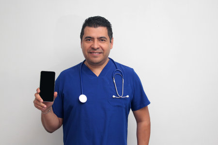 Dark-skinned Latino male doctor with a stethoscope shows his cell phone to have online consultations with his patientsの写真素材
