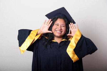 Young 25-year-old brunette Latina woman wearing a cap and gown to celebrate her graduation, proud,...