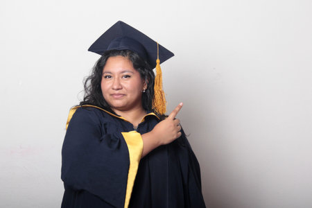 Young brunette Latina woman wearing a cap and gown celebrates her graduation and the completion of...