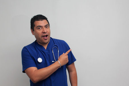 Dark-skinned Latino male specialist doctor with a stethoscope points with his finger with an expression of joy and surpriseの写真素材