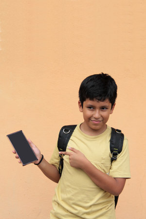 A 10-year-old Latino boy uses his cell phone to play video games, make video calls, send messages,...