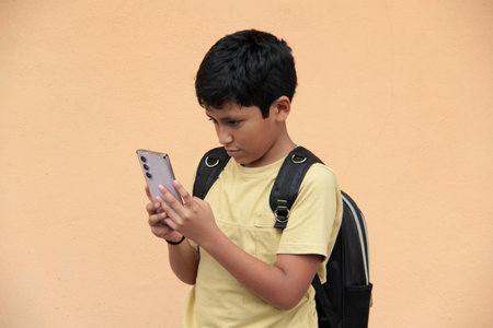 A 10-year-old Latino boy uses his cell phone to play video games, make video calls, send messages,...