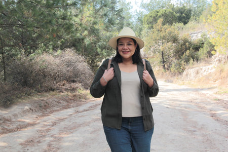 A 40-year-old Latina woman hikes in the mountains to fully enjoy nature and sunlight, experiencing well-being and empowermentの写真素材