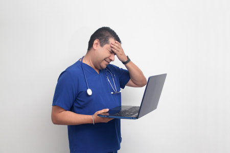 A dark-skinned Latino male specialist doctor uses a laptop to work on video call consultations,...