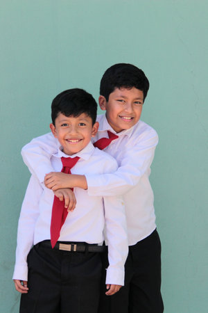 Two dark-skinned Latino male classmates dressed in uniform are excited and happy to be back in schoolの写真素材