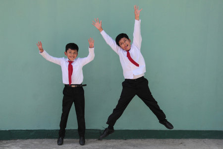Two dark-skinned Latino male classmates dressed in uniform are excited and happy to be back in schoolの写真素材