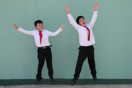Two dark-skinned Latino male classmates dressed in uniform are excited and happy to be back in schoolの写真素材