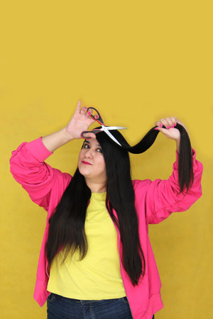 Adult Latina woman with long straight hair uses scissors to cut due to split endsの写真素材