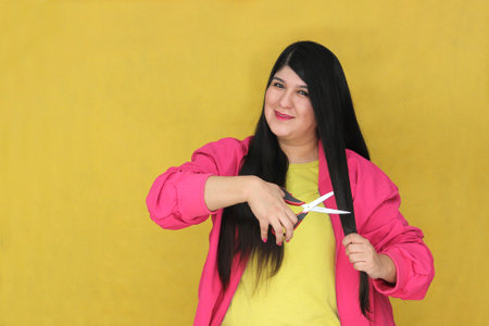 Adult Latina woman with long straight hair uses scissors to cut due to dehydration and split endsの写真素材
