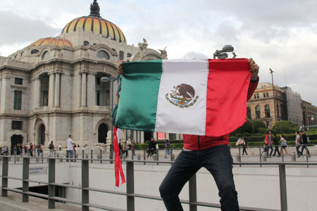 Mexico City, Mexico - Aug 23, 2023: Man proudly raises the Mexican flag in front of the Palacio de Bellas Artes in downtown CDMXのeditorial素材