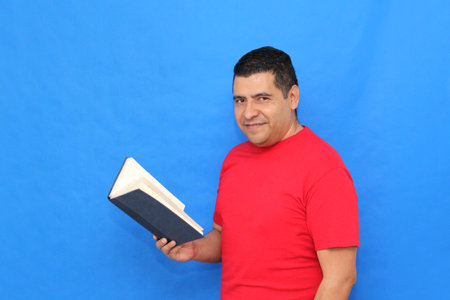 Dark-skinned Latino man shows and reads a book to learn and gain knowledge as a student and teacherの写真素材