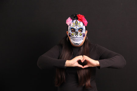 Woman wearing a skull mask makes a heart sign to remember her loved ones on the Day of the Dead in...
