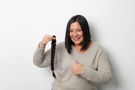 An adult Latina woman shows off the braid of hair she cut to donate for oncological wigs for girls with cancer and chemotherapy treatmentの写真素材
