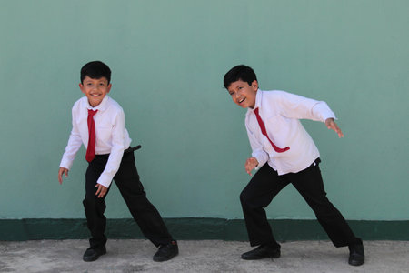 Two dark-skinned Latino male classmates dressed in uniform are excited and happy to be back in...