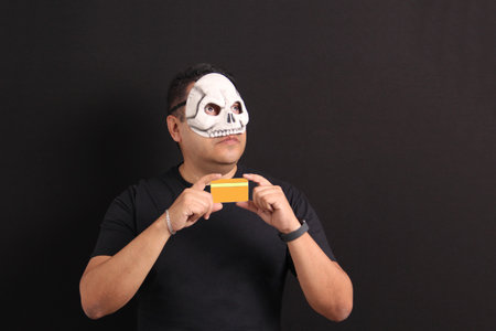 Man wearing a skull mask shows credit card to make purchases to celebrate the Day of the Dead in...