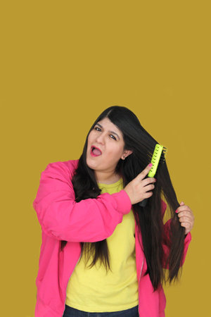 30-year-old Latina woman brushes her long, straight hair, suffering from damaged, dehydrated, and...