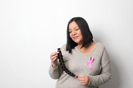 Adult Latina woman with a braid of hair she cut to donate for oncological wigs for women undergoing...