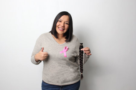 Adult Latina woman with a braid of hair she cut to donate for oncological wigs for women undergoing...