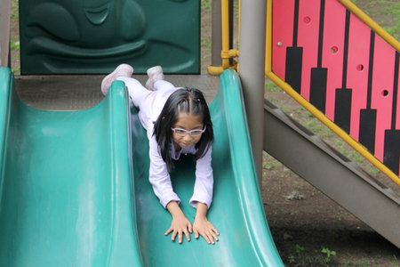 5-year-old Latina brunette girl with glasses plays on public playground equipment alone as therapy for ADHDの写真素材