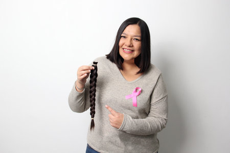 Adult Latina woman with a braid of hair she cut to donate for oncological wigs for women undergoing...