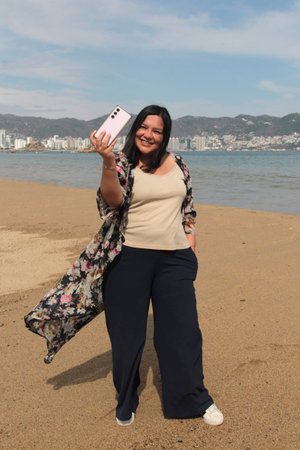 40-year-old Latina woman takes selfies alone and calmly while walking along the beach during her...