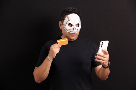 Mexican man wearing a Catrin Calavera mask uses his cell phone and credit card to make purchases to celebrate the Day of the Dead in Mexicoの写真素材