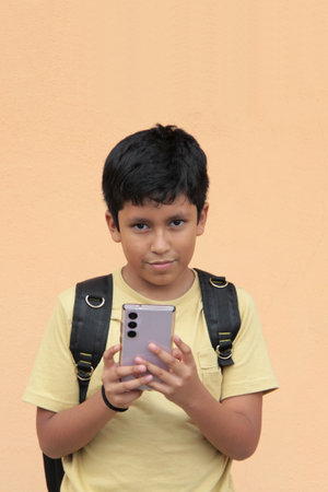 10-year-old Latino boy uses his cell phone to play video games, make video calls, send messages, and...
