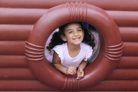4-year-old Latina girl with brunette hair and curly hair plays alone on outdoor playground equipmentの写真素材