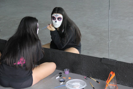18-year-old Mexican woman puts on catrina skull makeup in front of the mirror to celebrate the Day...