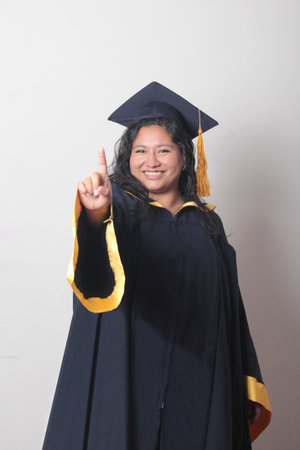 Young brunette Latina woman wearing a cap and gown celebrates her graduation and the completion of her studiesの写真素材