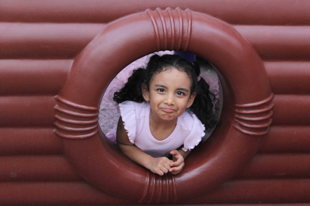 4-year-old girl with brunette hair and curly hair plays alone on outdoor playground equipmentの写真素材