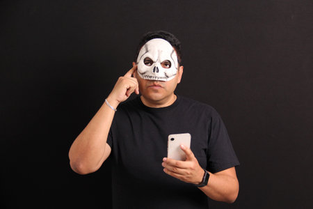 Mexican adult man with skull mask uses his cell phone to take advantage of Day of the Dead promotions and discounts in Mexicoの写真素材