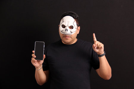 Mexican adult man with skull mask uses his cell phone to take advantage of Day of the Dead promotions and discounts in Mexicoの写真素材