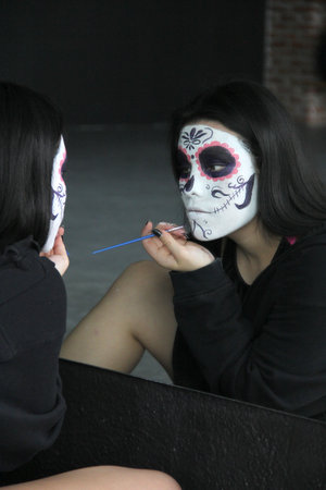 Young Mexican woman puts on catrina makeup in front of the mirror to celebrate the Day of the Dead...