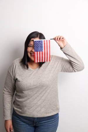 40-year-old Latina woman proudly displays the United States flag as a symbol of migration and...