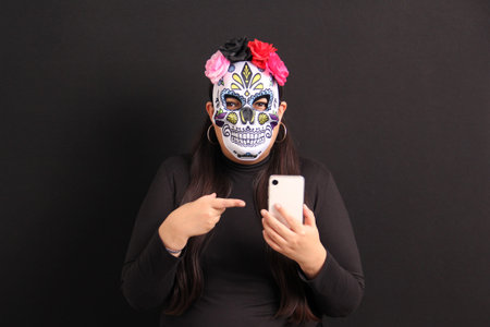 Mexican adult woman with Catrina mask shows her cell phone to see Day of the Dead promotions and discounts in Mexicoの写真素材