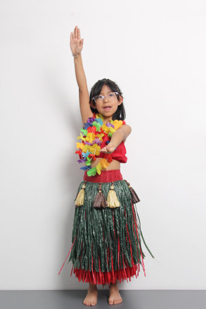 5-year-old Latina girl with brown hair enjoys learning to dance Hawaiian, wearing a colorful skirt and leis, and shows off her movesの写真素材