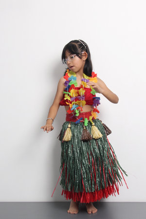 5-year-old Latina girl with brown hair enjoys learning to dance Hawaiian, wearing a colorful skirt and leis, and shows off her movesの写真素材
