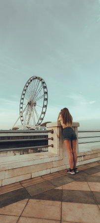 A young woman stands on the promenade and looks at the ferris wheel.の写真素材