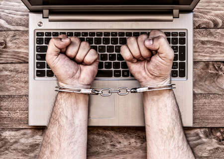 Handcuffed hands in front of the computer making reference to web-crimes.