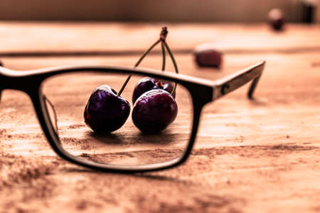 Red cherries seen through a pair of glasses, on a wooden tableの写真素材
