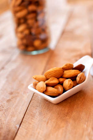 Almonds on a white ceramic spoon, on a wooden background.の写真素材