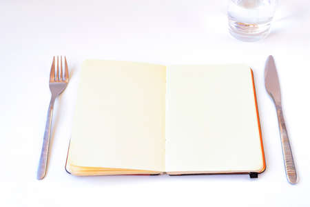 Diets concept. Open notebook on the table with plate, cutlery and glass of water; with white...