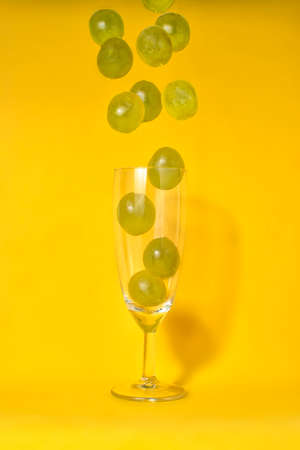 Grapes falling into a champagne glass with yellow backgroundの写真素材