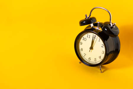Black alarm clock on yellow background. Concept time.の写真素材