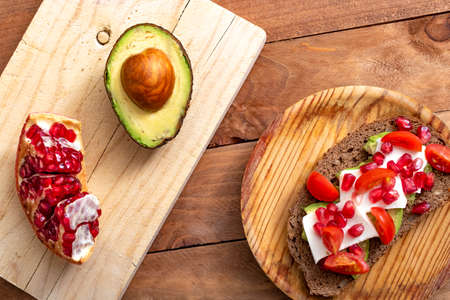 Slice of bread with avocado, cherry tomato and pomegranate seeds, on wood.Slice of bread with avocado, cherry tomato and pomegranate seeds, on wood.の写真素材